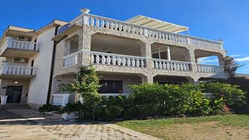 A two-story building with a stone facade, balconies with white railings, and a clear blue sky.