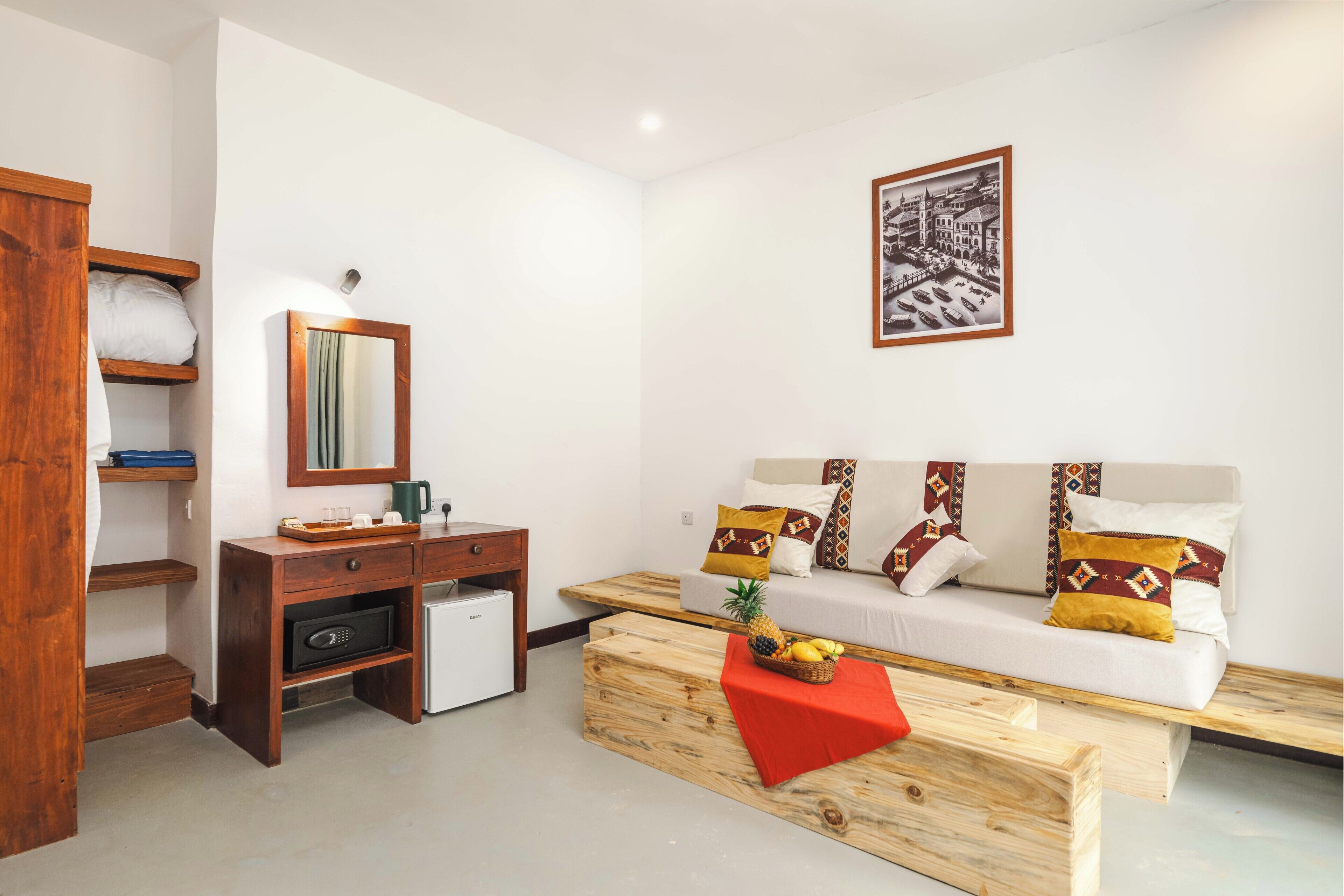 Una habitación moderna con sofá, una mesita de centro con fruta, un refrigerador pequeño y un escritorio de madera.