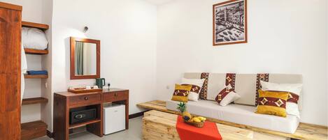 Una habitación moderna con sofá, una mesita de centro con fruta, un refrigerador pequeño y un escritorio de madera.