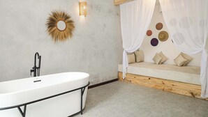 Un baño moderno con una bañera independiente, una lámpara de pared y un espejo decorativo con diseño de sol.
