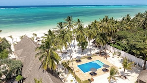 Vista de una playa con piscina, palmeras y cielo despejado.