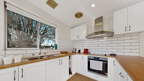 Una cocina moderna con armarios blancos, encimera de madera, ventana con vistas a árboles y horno empotrado.