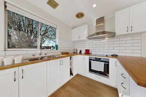 A modern kitchen with white cabinets, a wooden countertop, a window with a view of trees, and a built-in oven.