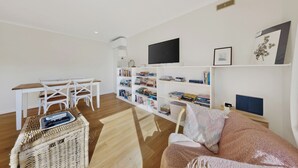Una sala de estar moderna con un sofá blanco, una mesa de comedor de madera, una silla blanca, una estantería y un televisor.