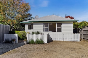 A single-story house with a white picket fence, a gravel driveway, and a metal roof.