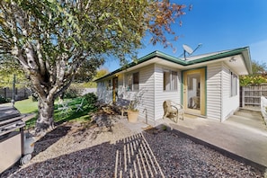 A small, single-story house with a green roof, a satellite dish, and a gravel driveway.