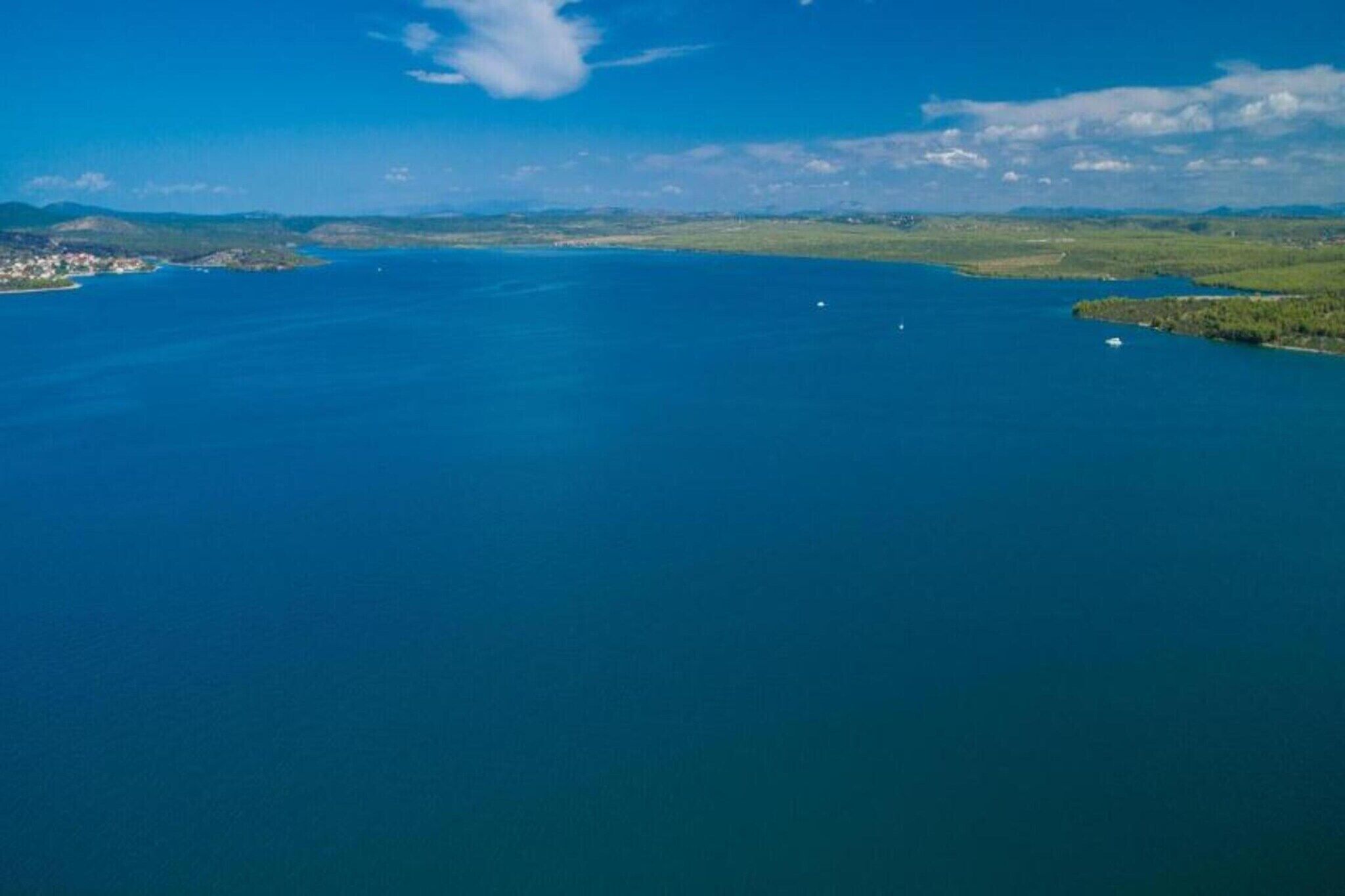 Vista aerea di una zona costiera con un ampio specchio d'acqua, una piccola isola e una costa lontana con edifici.