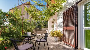 Une terrasse avec deux chaises et une table, entourée de plantes en pot et d’un bâtiment dont le volet est de couleur marron.