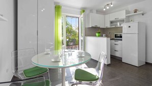Une cuisine moderne avec des armoires blanches, un four encastré et un réfrigérateur. On y trouve également un coin repas avec une table et des chaises en verre.