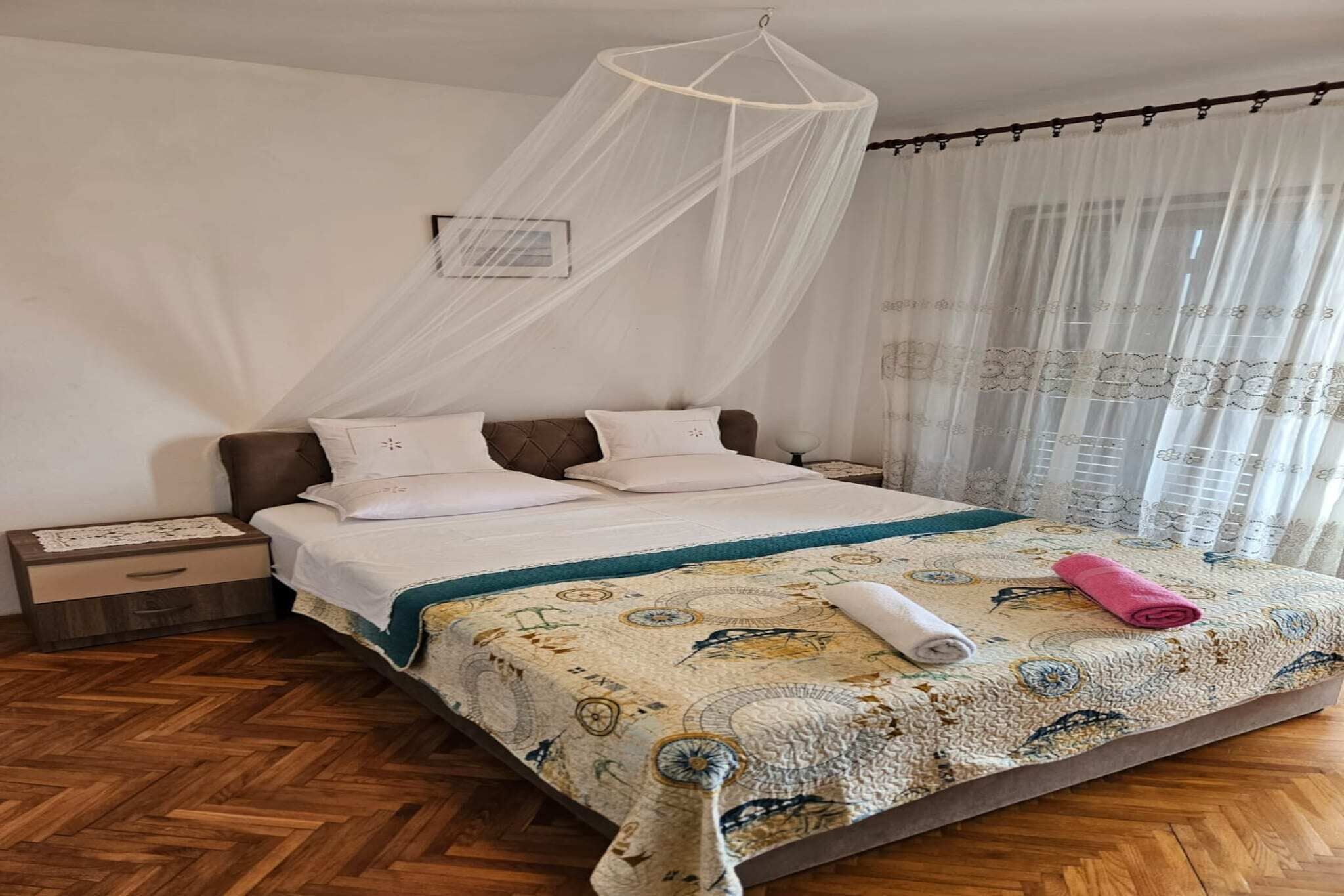 Una cama bien hecha con una colcha estampada, un dosel blanco y suelo de madera.