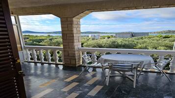 Un espacio al aire libre cubierto con una mesa y sillas, vistas a zonas verdes y edificios a lo lejos, y piso de baldosas.