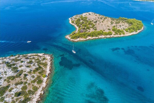 An aerial view of a small island with clear blue waters and a boat anchored nearby.