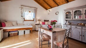 Een gezellige kamer met een houten plafond, een bed met een witte hemel, een eettafel met stoelen en een keukenhoek met kastjes.