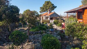 Een landelijke stenen woning met pannendak, omgeven door een tuin met diverse planten en bomen.