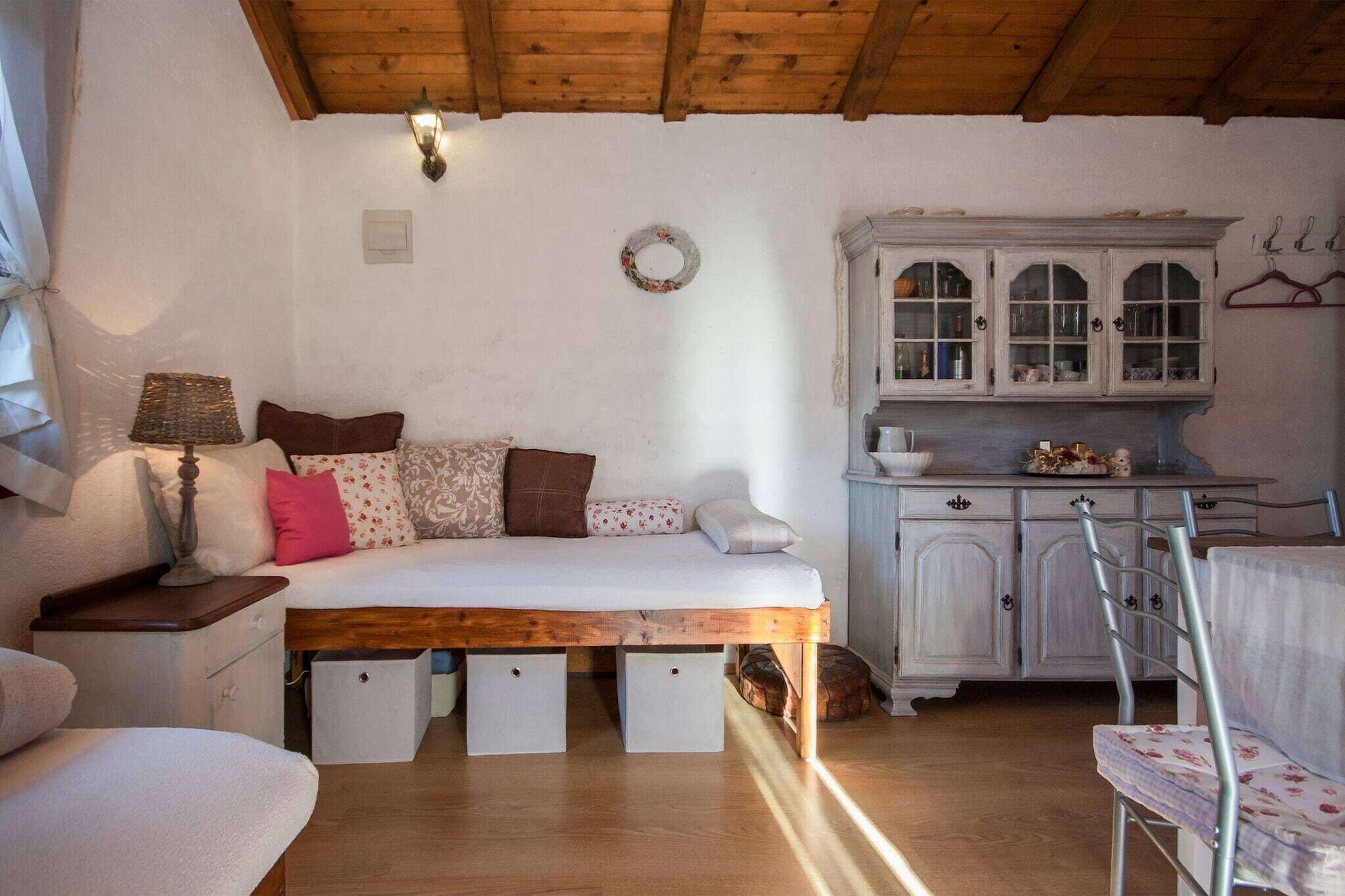 A cozy room with a wooden bed, a white sofa, a small table with a lamp, and a white cabinet with glass doors.
