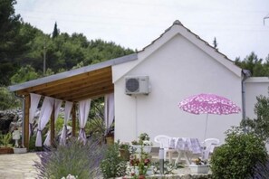 Un bâtiment blanc avec un toit en pente, un patio couvert avec une table et des chaises, et un parasol rose.