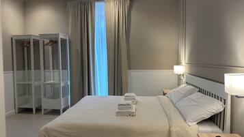 A hotel room with a bed, a nightstand, a lamp, a wardrobe, and a window with curtains.