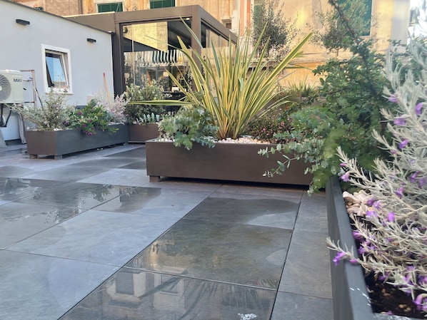 A courtyard with tiled flooring, planters with various plants, and a modern building facade. - TERRAZZA CARBONARA B&B (Naples)