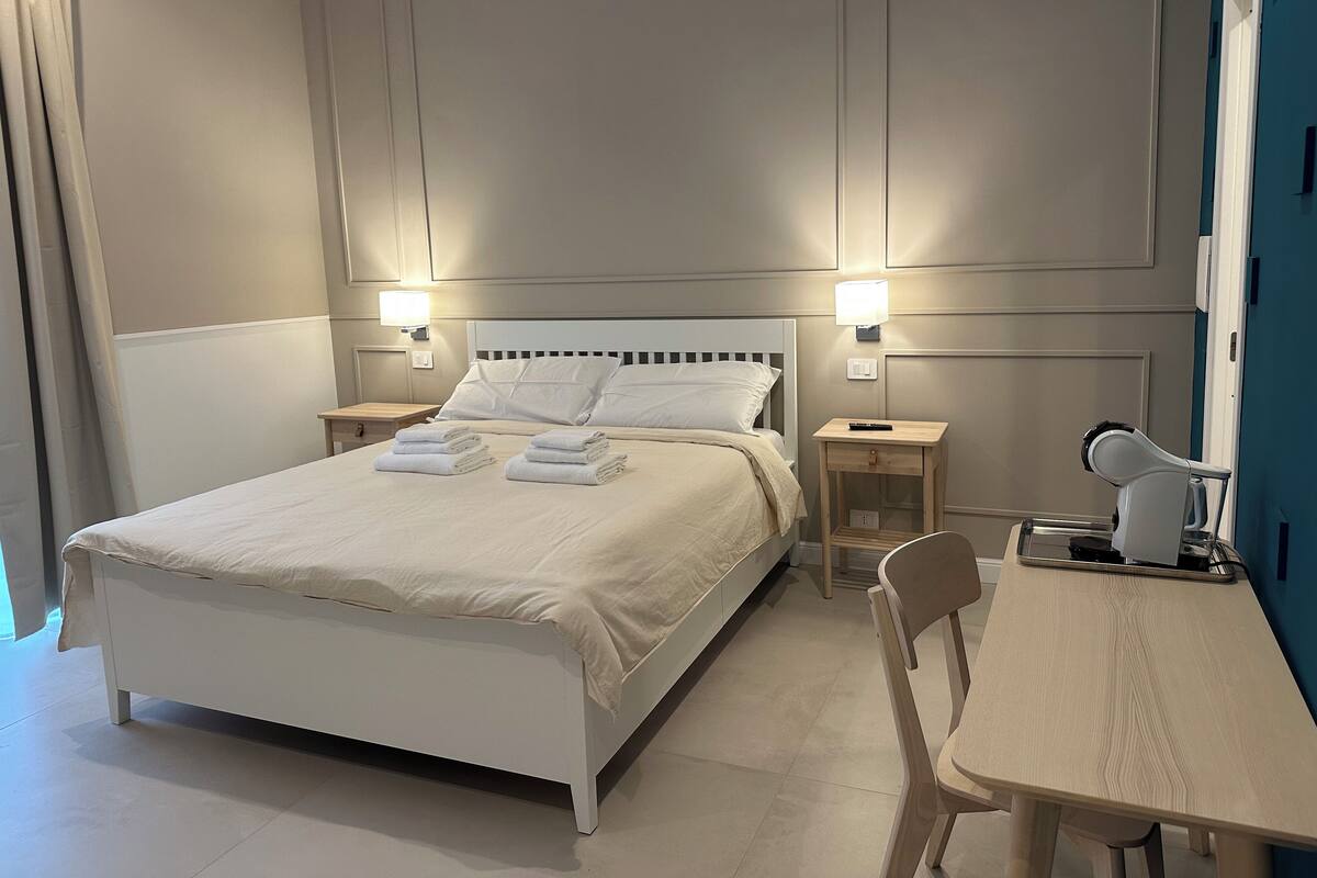 Ein Hotelzimmer mit einem großen Bett, zwei Nachttischen mit Lampen, einem Schreibtisch mit Stuhl und einem Spiegel.