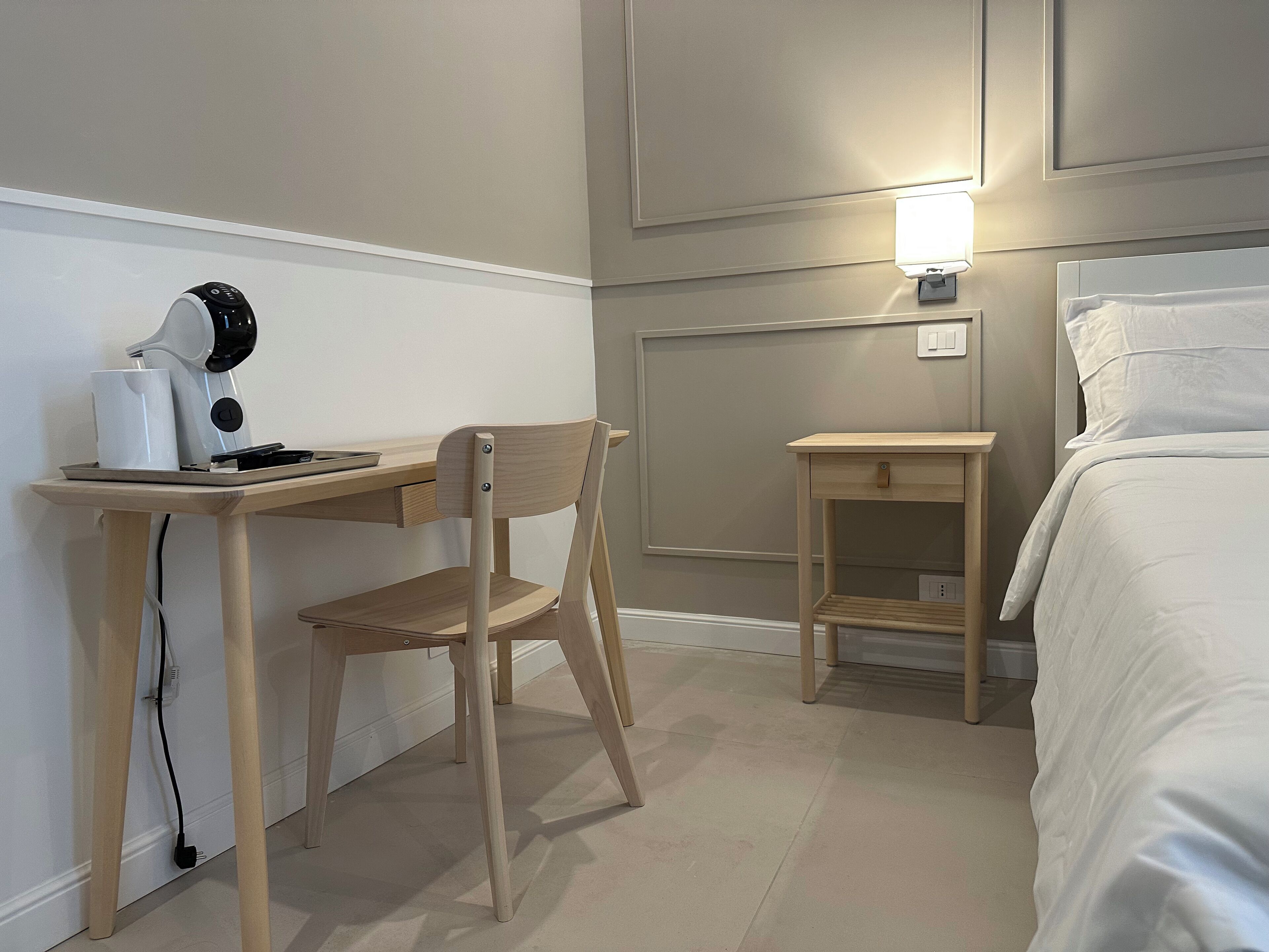 Ein Hotelzimmer mit Holztisch, Stuhl, Nachttisch, Lampe und Bett.