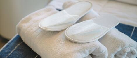 A neatly folded white towel and a pair of white slippers on a bed with a blue striped pillow.