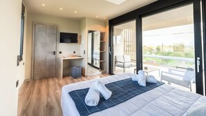 A modern hotel room with a large bed, a desk, and a balcony with outdoor seating. - Grand Kourouta Pool Apartments (Ilida)