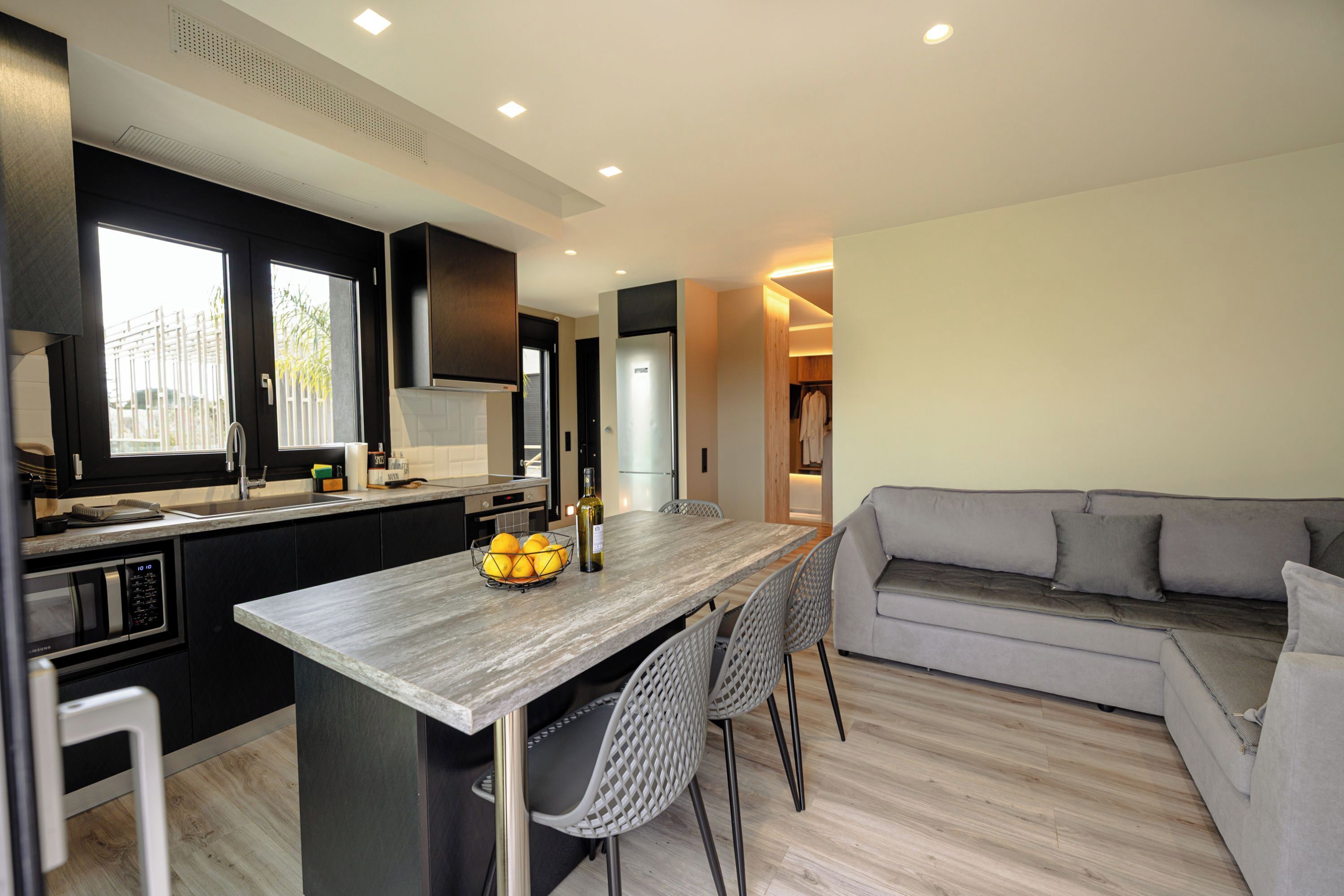 A modern kitchen with a central island, black cabinets, and a grey sofa in the living area.