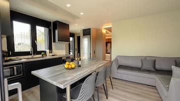 A modern kitchen with a central island, black cabinets, and a grey sofa in the living area.