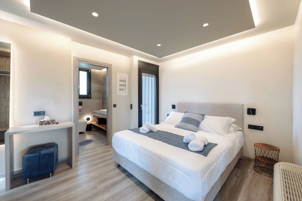 A modern bedroom with a large bed, bedside tables, a desk, and a small seating area.