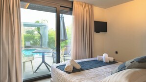 A hotel room with a bed, a TV, a view of an outdoor pool, and a table with chairs. - Grand Kourouta Pool Apartments (Ilida)