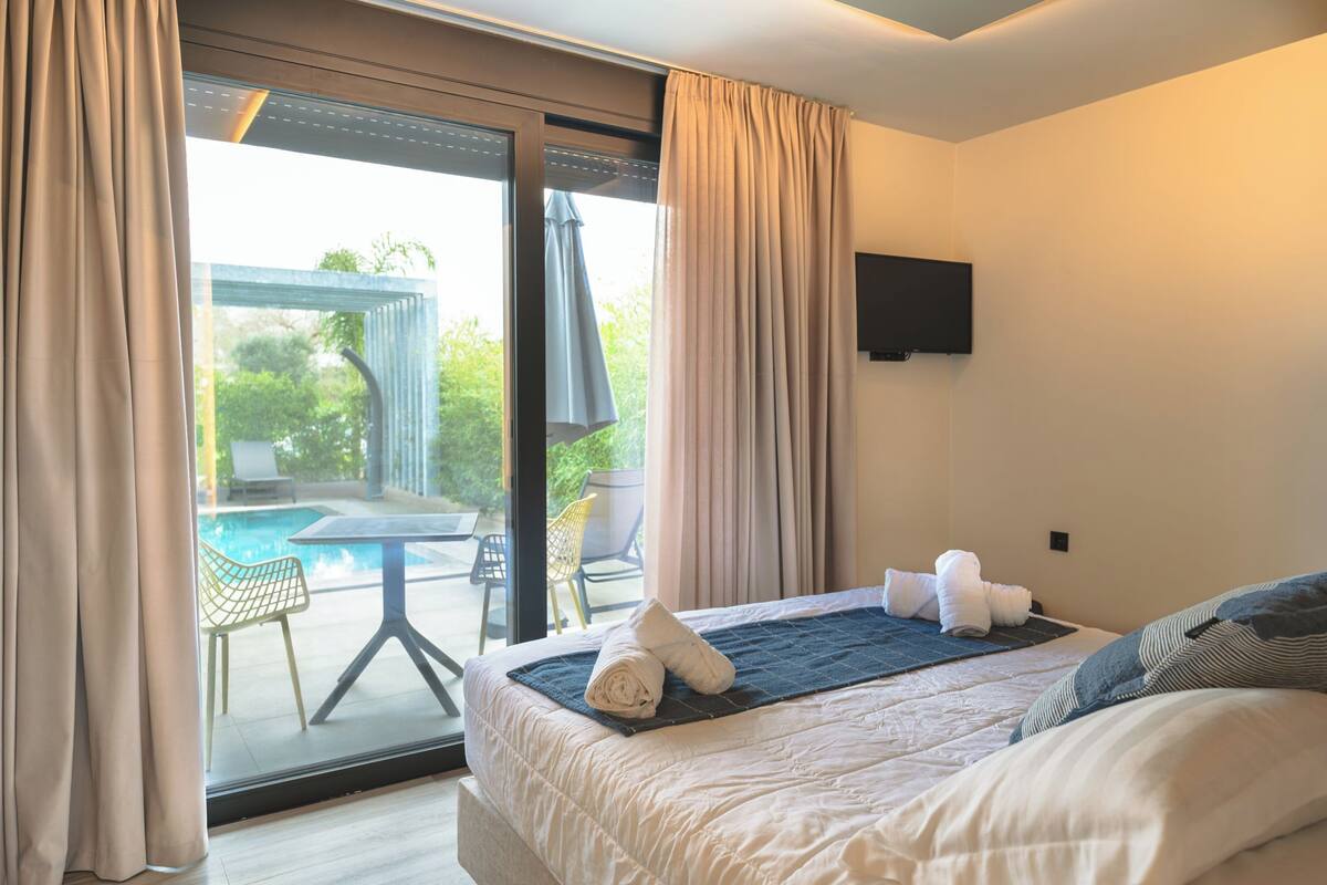 A hotel room with a bed, a TV, a view of an outdoor pool, and a table with chairs.