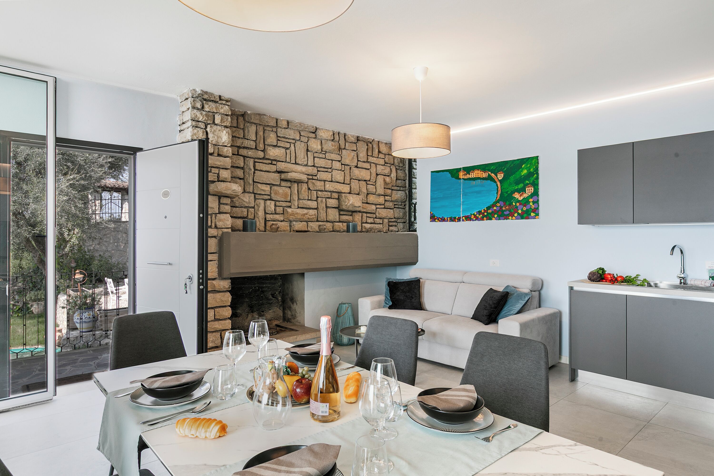 Un comedor moderno con chimenea de piedra, una mesa de comedor lista para una comida y una cocina con armarios grises.
