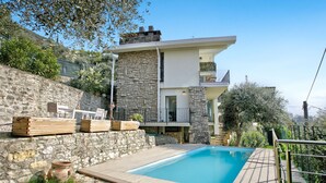 Una casa moderna de dos pisos con fachada de piedra, una terraza de madera y una piscina.