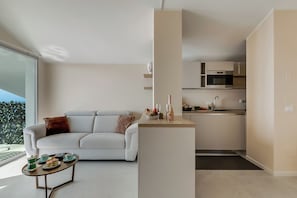 A modern living room with a sofa, a coffee table with tea cups and pastries, and a kitchen area with a microwave and cabinets. - Villa Mercurio Apartments (Brenzone sul Garda)
