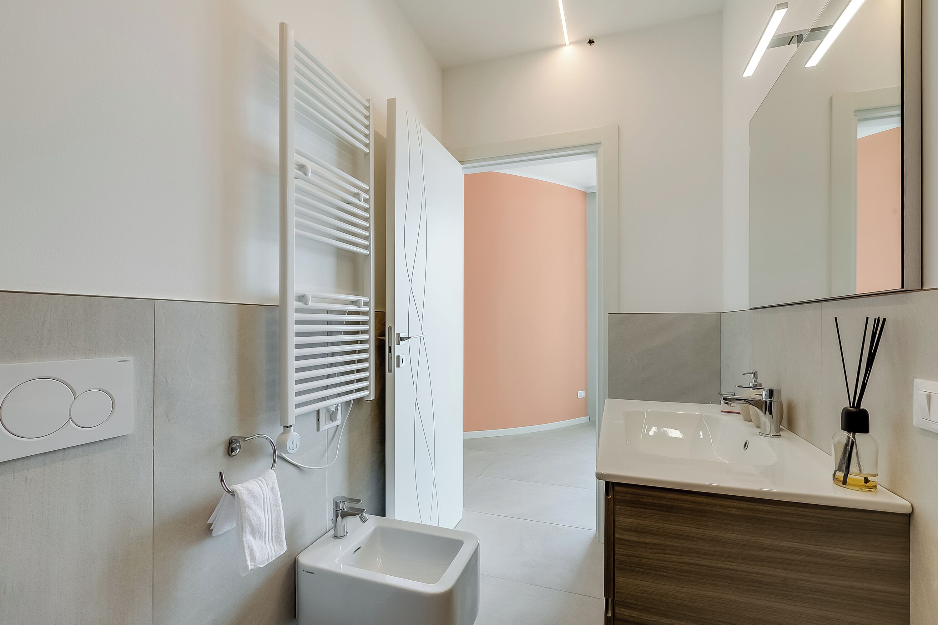 A modern bathroom with a sink, mirror, towel rack, and a toilet.