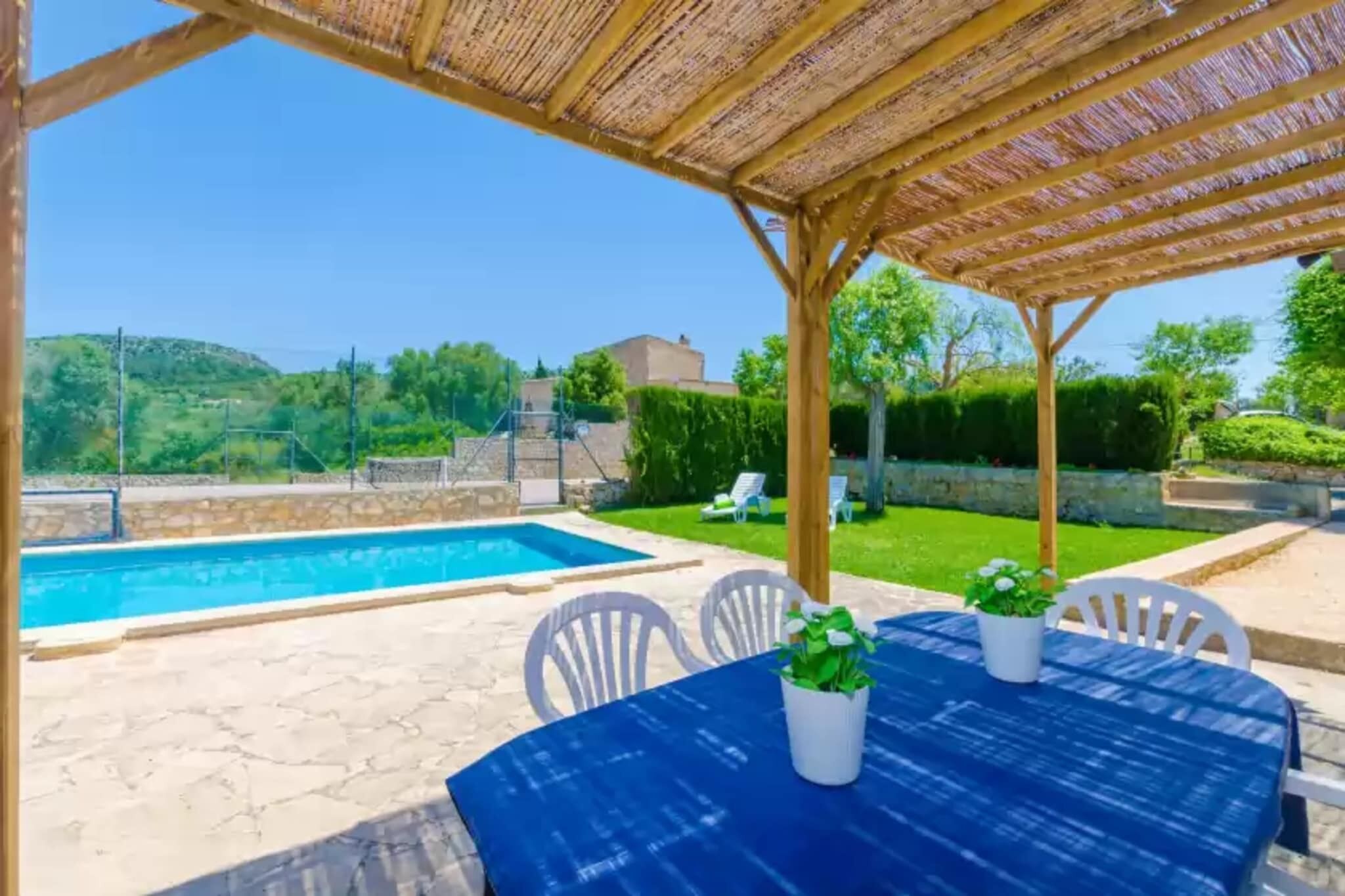 A covered outdoor area with a pool, white chairs, and a table with potted plants.