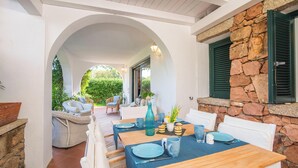 An outdoor patio area with a stone wall, wooden table, and white chairs.