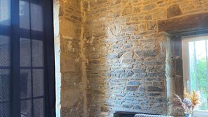 A rustic stone-walled room with a bed, a chandelier, and a window with natural light. - For group 🌟 (Saint-Cyr-en-Pail)