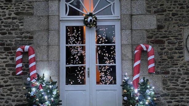 A stone building with a white door, two Christmas trees, and candy canes. - For group 🌟 (Saint-Cyr-en-Pail)