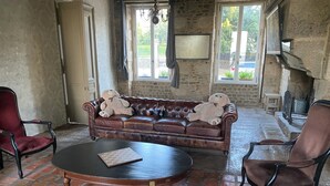 A room with a brown leather sofa, two armchairs, a round wooden coffee table, and a stone wall. - For group 🌟 (Saint-Cyr-en-Pail)
