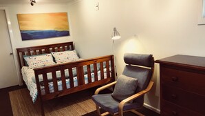 A bedroom with a wooden bed, a gray chair, a dresser, and a painting on the wall.