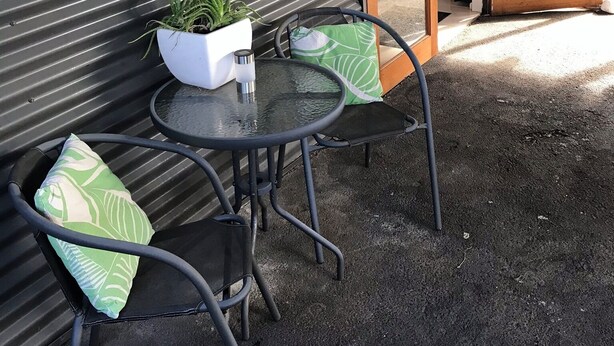 An outdoor seating area with a metal table and chairs, a potted plant, and a sliding glass door leading to a garden.