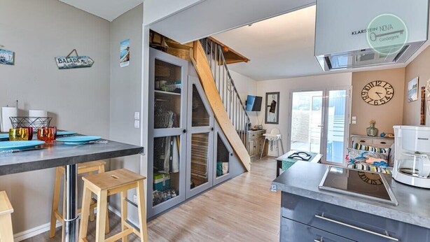 Une cuisine moderne avec un escalier en bois, un coin repas avec des tabourets et un plan de travail équipé de divers appareils électroménagers.