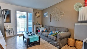 Un salon avec un canapé gris, une table basse, une horloge et une vue sur l’extérieur.