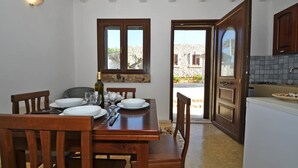 A dining area with a wooden table set for four, a bottle of wine, and a view of the outside.