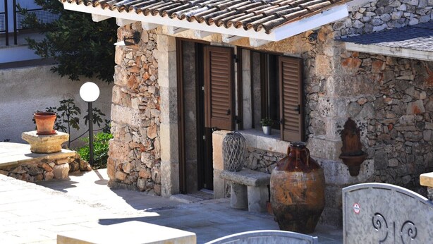 A stone building with a tiled roof, a bench, and a large vase.