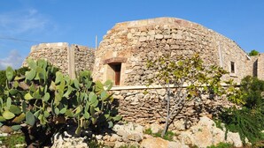 A stone building with a circular structure, a small window, and a tree in the foreground.