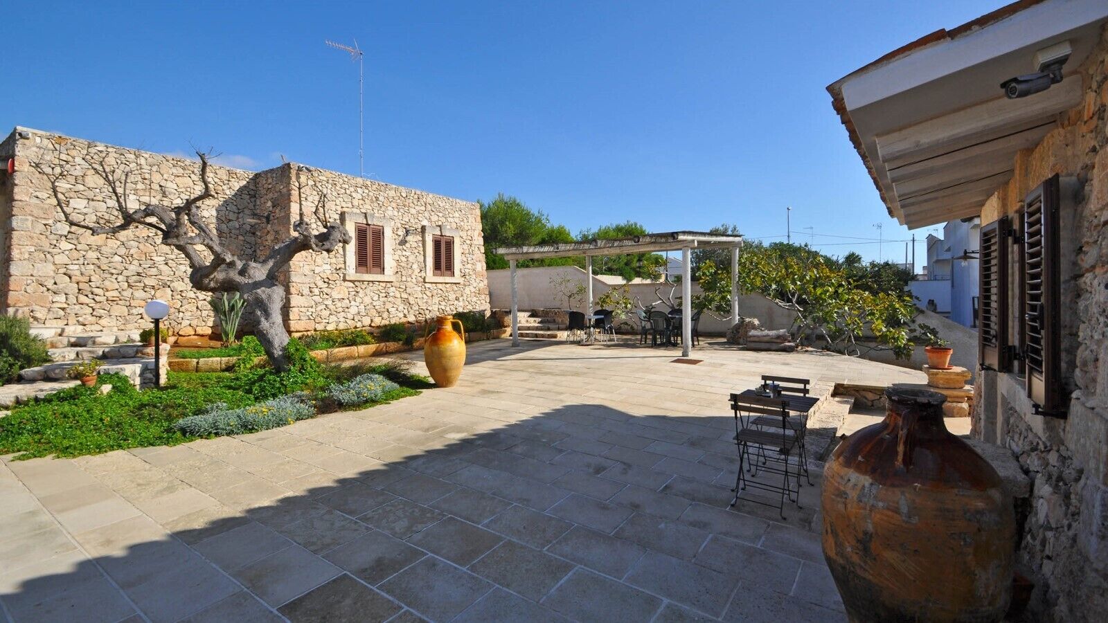 A stone building with a tiled patio, outdoor furniture, and large vases.