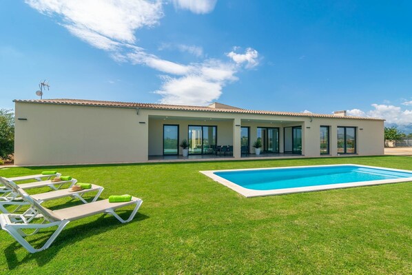 Une maison moderne dotée d’une piscine, d’un patio couvert et d’une pelouse aménagée avec des chaises longues.