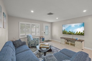 A living room with a large flat-screen TV, a sofa, a patterned armchair, and a glass coffee table. - 'Coral Breeze' home Near Siesta Key! Pool (Sarasota)
